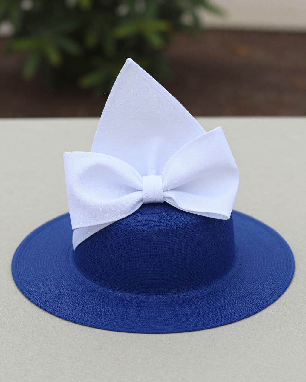 Cobalt blue Derby hat with a large white bow on a neutral tabletop.