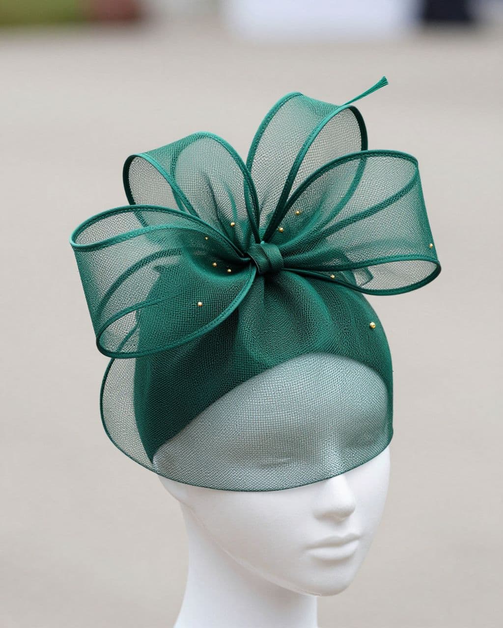 Emerald green fascinator with a spiral mesh bow and tiny gold accents.