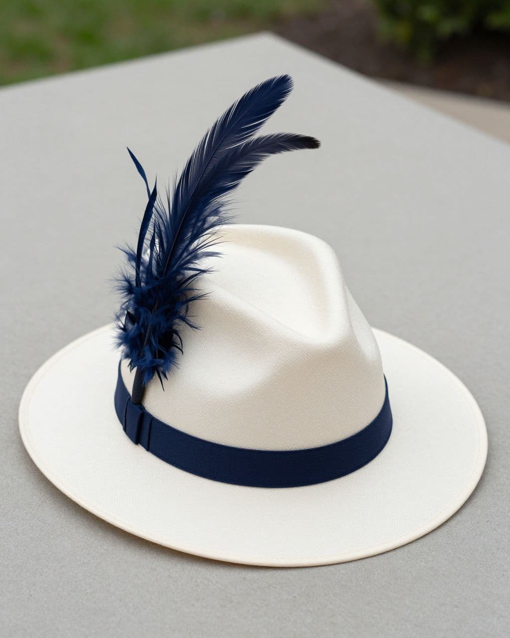 Ivory Derby hat with a sweeping navy feather on a neutral tabletop.