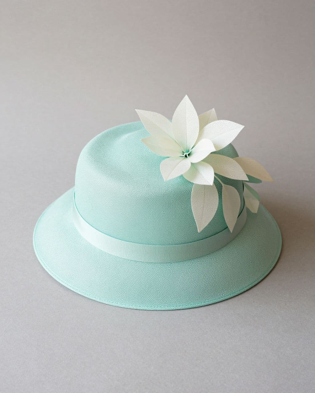 Mint green cloche hat with ivory fabric leaves on a neutral tabletop.