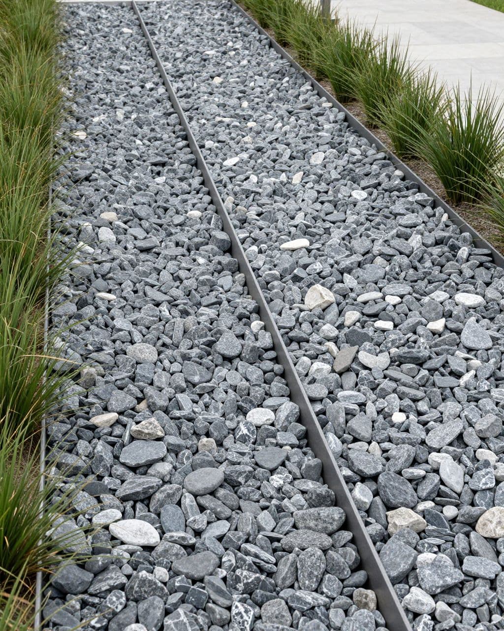 A stone-lined dry creek bed with steel edging crosses a minimalist backyard.