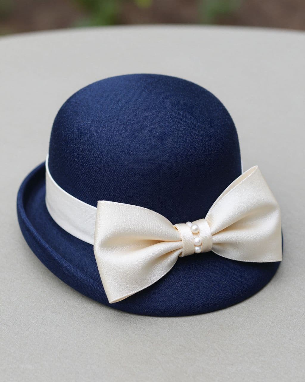 Navy pillbox hat with an ivory bow and pearl-like accents on a tabletop.