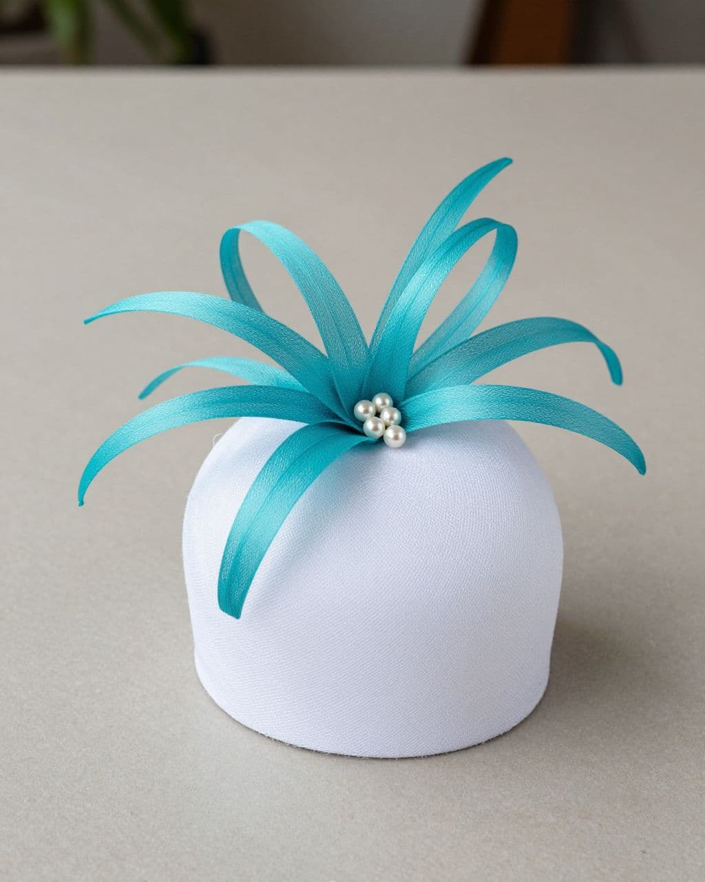 White fascinator with turquoise loops and pearl-like beads on a neutral tabletop.
